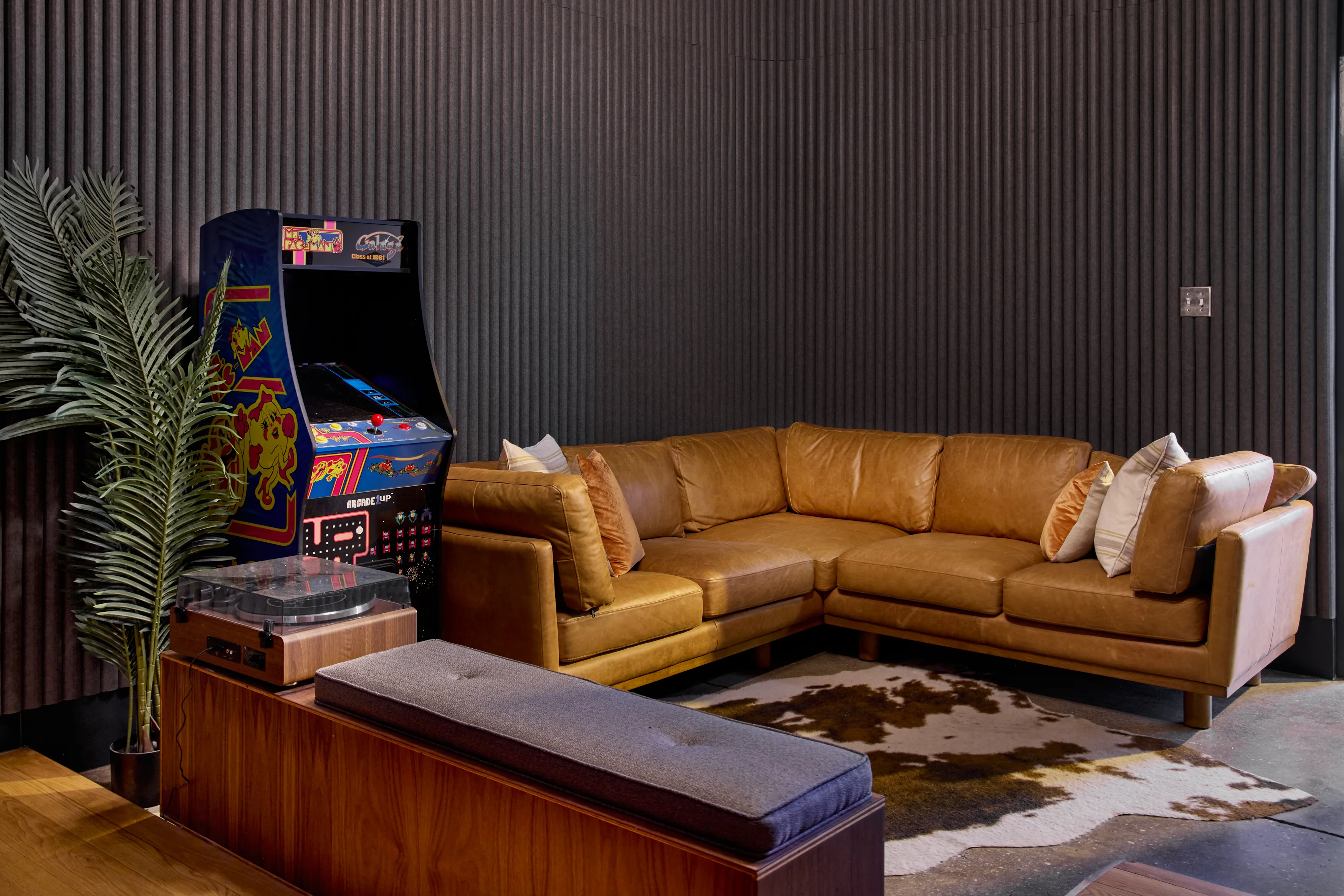 Wide shot showing a plant, arcade machine, wrap around couch, and dark, textured walls