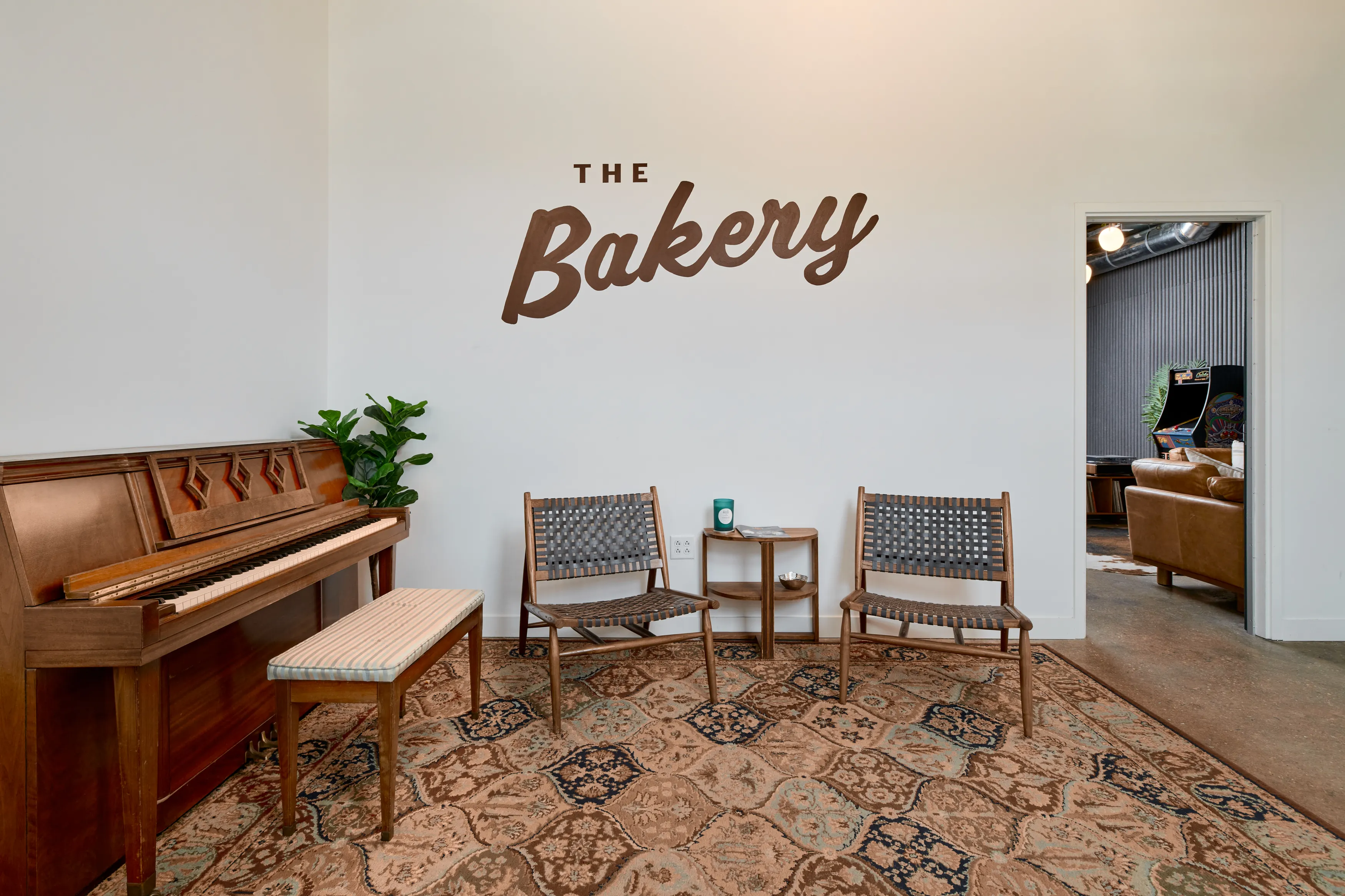 The Bakery recording studios lobby with the logo on the wall, a vintage piano, and two lounge chairs on a rug